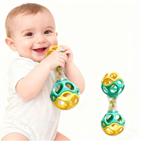 A smiling baby is holding a green and yellow rubber teething rattle toy.