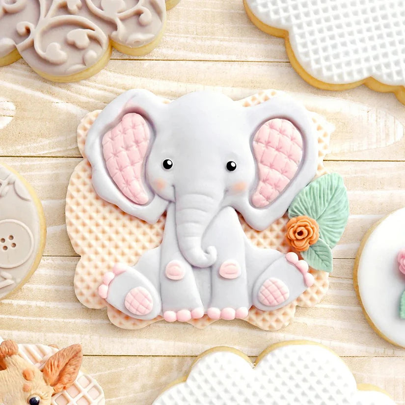 A collection of elephant silicone baking molds in various shades of gray and pink resting on a light wooden surface.