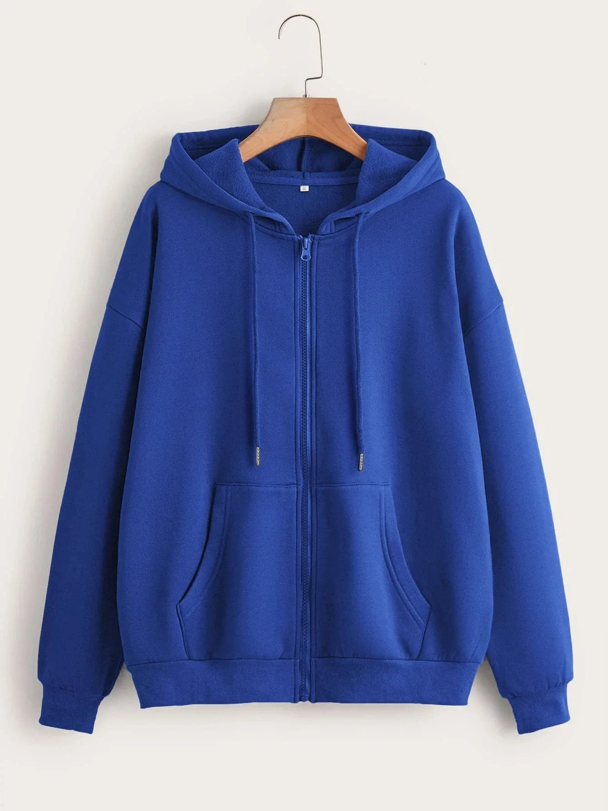 A royal blue oversized zip-up hoodie with a hood and front pocket hanging on a wooden hanger.