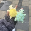A hand is holding a yellow and green mini turtle plush chew toy against a gray background.