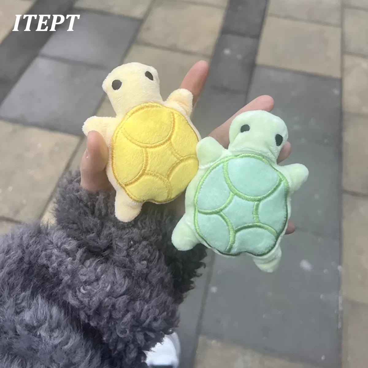 A hand is holding a yellow and green mini turtle plush chew toy against a gray background.