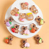 A collection of small resin figurines depicting capybaras holding various fruits and honey on a white plate.