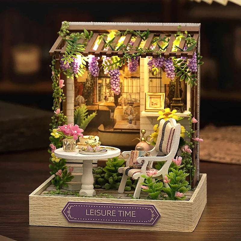 A miniature dollhouse puzzle kit featuring a wooden frame decorated with greenery and purple flowers.