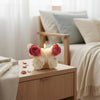 A white rose butterfly silicone mold sits on a wooden surface next to a lit candle in a bright, soft-lit room.