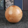 A round wooden puzzle ball with geometric cuts resting on a dark gray carpet.