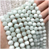 A hand is holding a strand of small, round, pale green and white natural stone beads for jewelry making.
