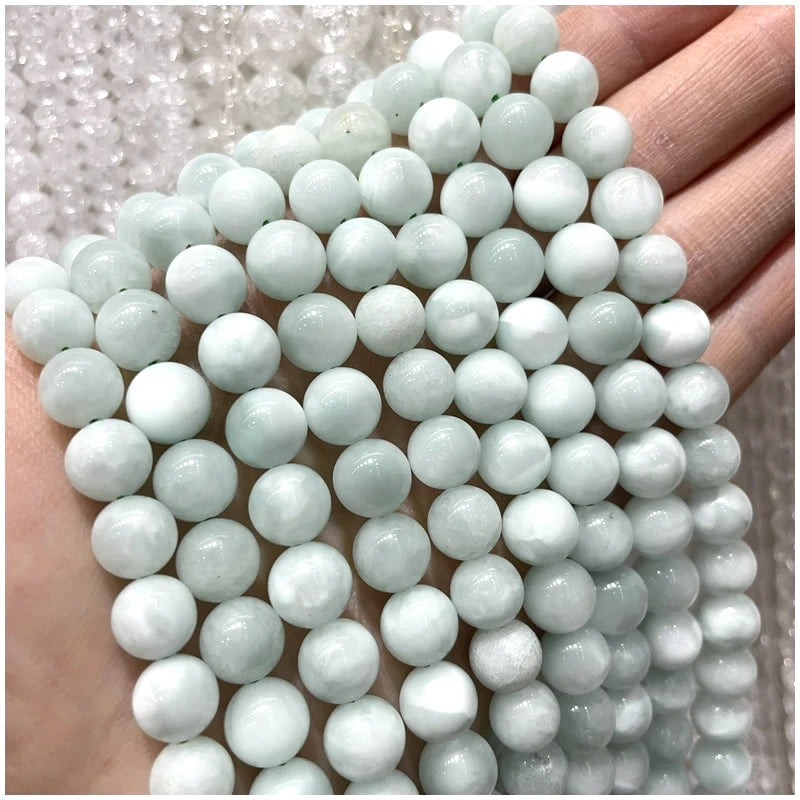 A hand is holding a strand of small, round, pale green and white natural stone beads for jewelry making.