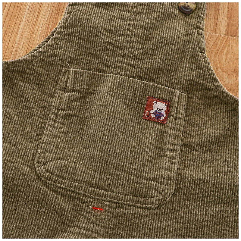 A close-up of olive green corduroy baby cotton overalls with a patch featuring a white bear.