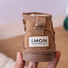 A pair of tan suede winter snow boots for toddlers is held in a hand.