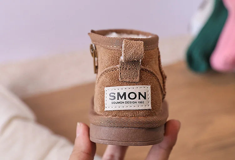 A pair of tan suede winter snow boots for toddlers is held in a hand.