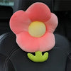 A pink plush lumbar support pillow shaped like a flower with a yellow center and green stem placed on a black car seat.