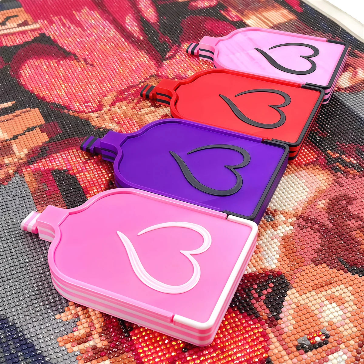 A collection of plastic storage trays in pink, red, and purple are displayed on a diamond painting fabric.