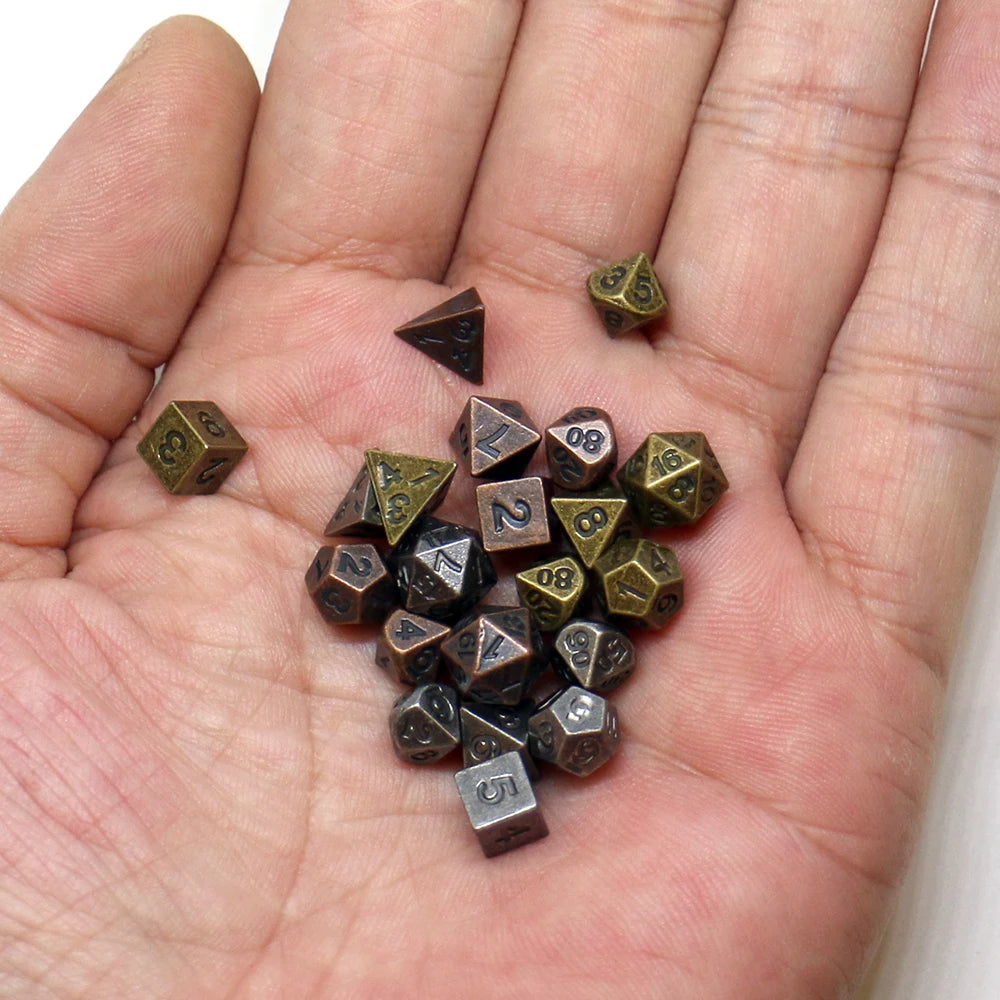A hand holds a set of seven antique metal polyhedral dice used for RPG games.