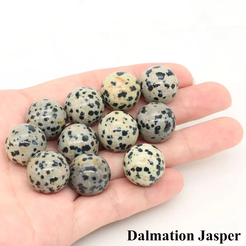 A collection of polished Dalmation Jasper spheres in various shades of gray and black on a hand.