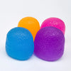 Three brightly colored soft squishy stress relief balls in orange, pink, and blue.