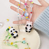 A hand holds a panda blind box collectible figure and various beaded jewelry on a white plate.