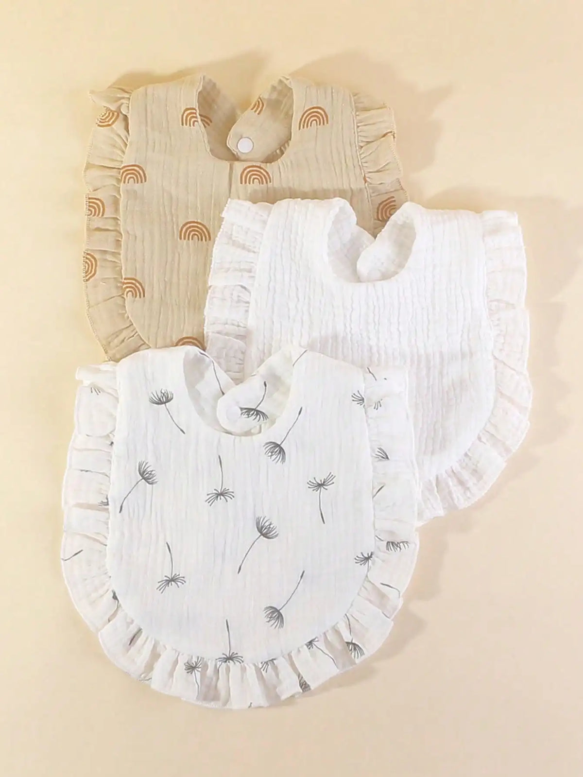 A set of three white muslin baby bibs with ruffled edges and small floral embroidery displayed on a light background.