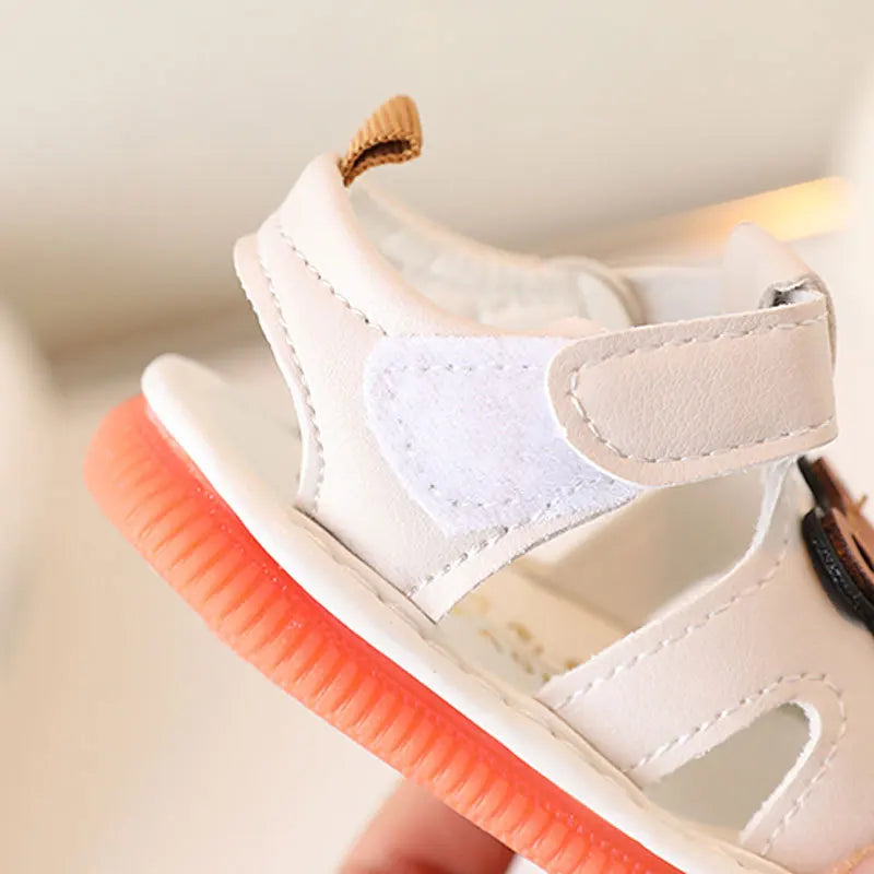 Sandale en similicuir blanc pour bébé avec semelle orange et bride marron.