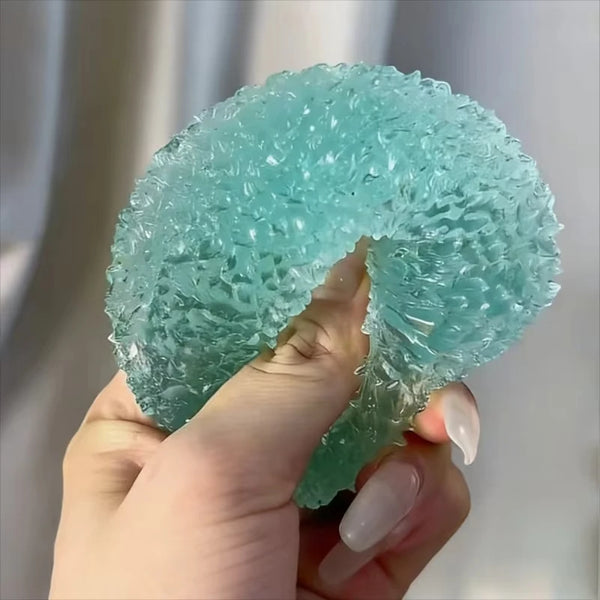 A hand holds a translucent, light blue squishy stress relief fidget toy.