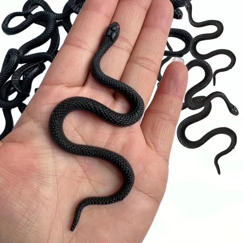 A hand is holding a realistic soft rubber black snake prop.