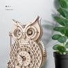 A restored wooden owl pendulum clock with intricate details displayed against a white wall.