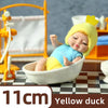A yellow duck mini reborn baby doll is shown resting in a white bowl on a checkered surface.