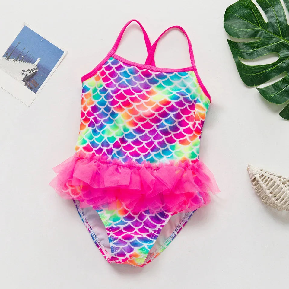 A vibrant, iridescent mermaid unicorn one-piece swimsuit featuring a scale pattern in pink, blue, and green.