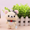 A fluffy white bear plush toy with pink ears and a black bow, standing in front of a green plant.