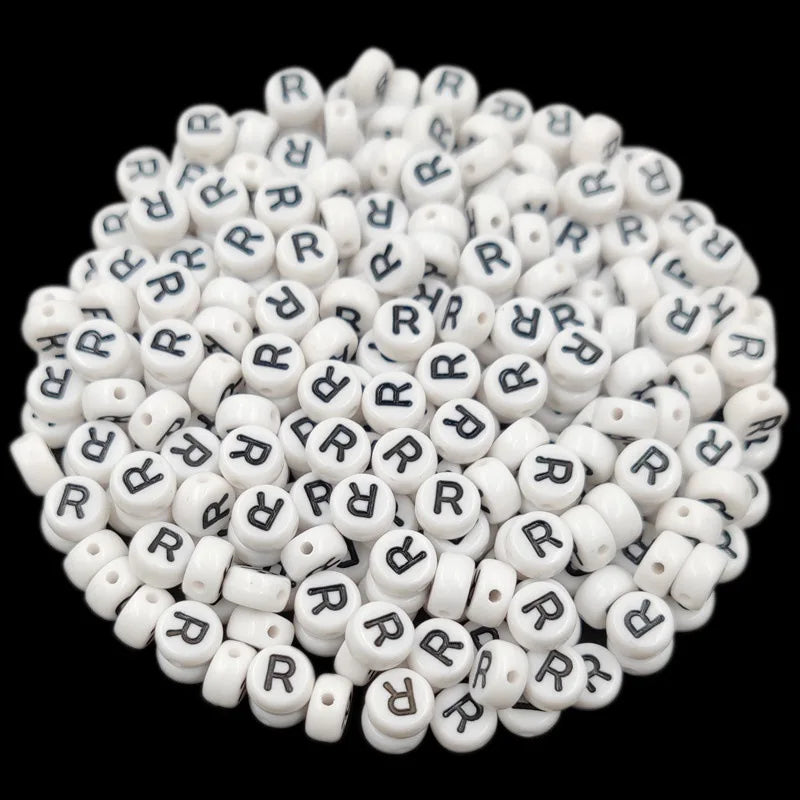 A pile of small white acrylic alphabet letter beads in various shapes and sizes.