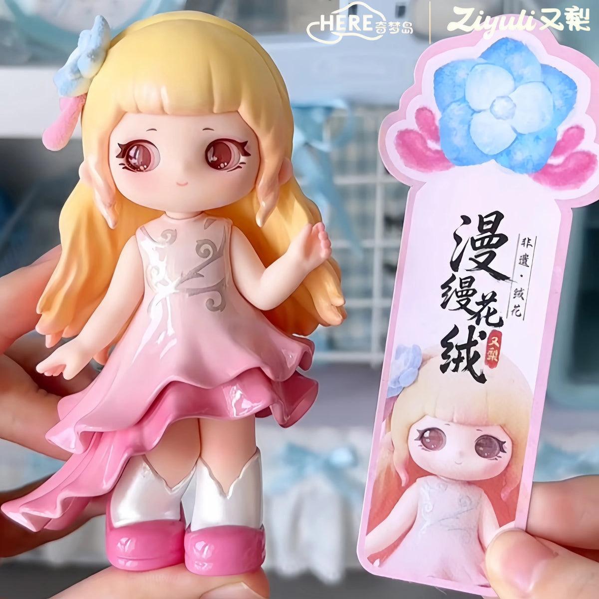 A figurine of a girl with long blonde hair and pink dress is held next to its packaging card.