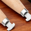 A close-up view of a professional bezel setting pusher tool with a silver metal head and a light wooden handle resting on a d