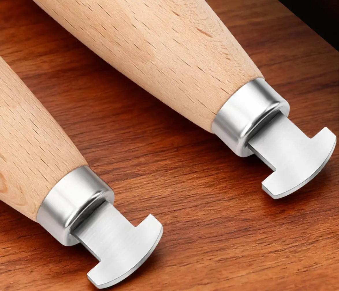 A close-up view of a professional bezel setting pusher tool with a silver metal head and a light wooden handle resting on a d