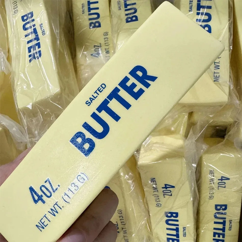 A hand holds a yellow butter squishy stress relief toy packaged in plastic bags.