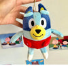A blue and white plush toy of a dog character, resembling Bluey, being held by a hand.