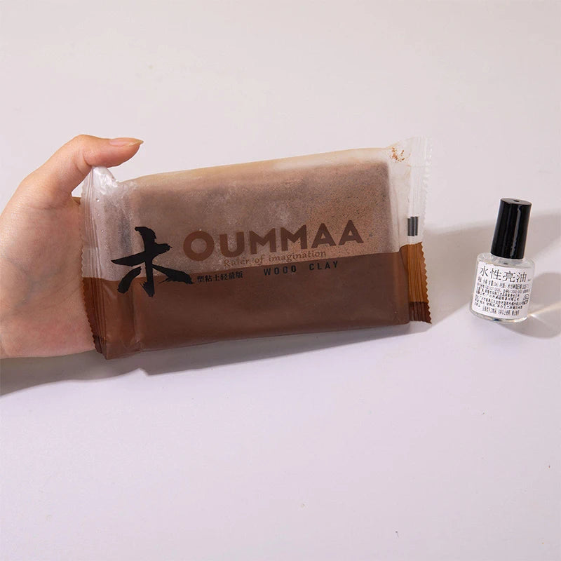 A hand holds a package of OUMMAA wood clay and a black cosmetic tube.