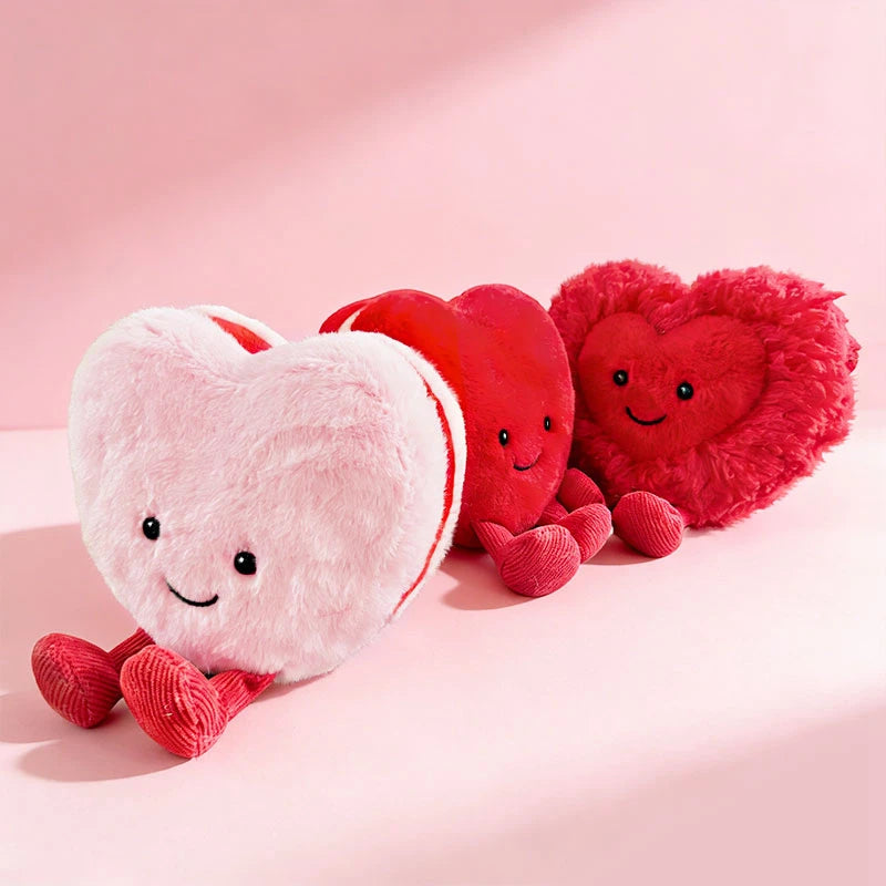 Three soft plush hearts in pink and red colors arranged on a light pink background.