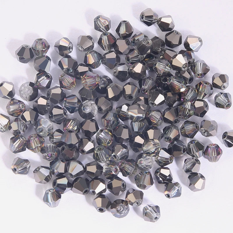 A pile of faceted crystal bicone glass beads in various shades of gray and clear, used for jewelry making.