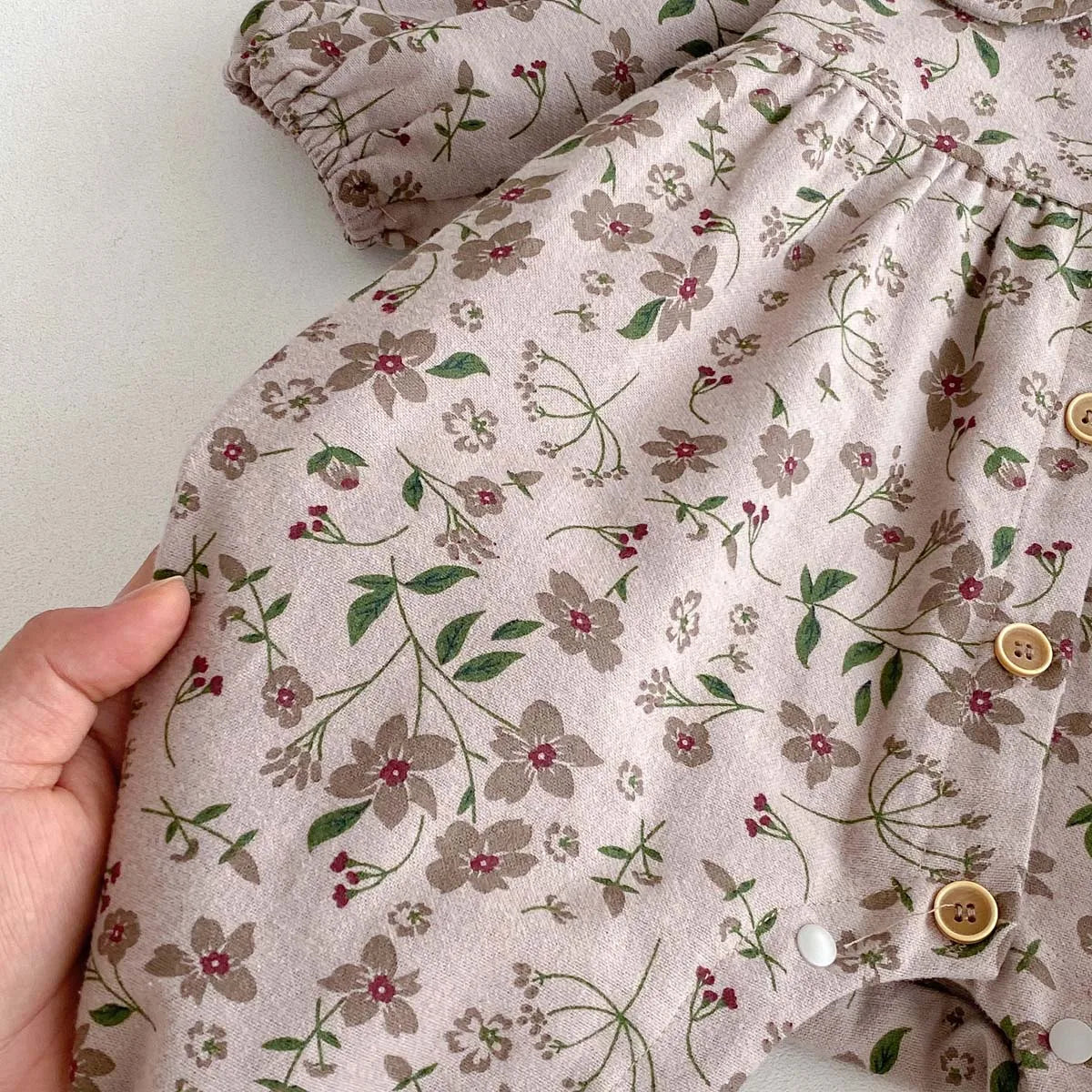 Close-up of a beige floral print baby girl long sleeve jumpsuit fabric with small embroidered flowers.