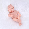 A realistic soft vinyl reborn baby doll wearing a matching pink patterned outfit and hat, lying on white fur.