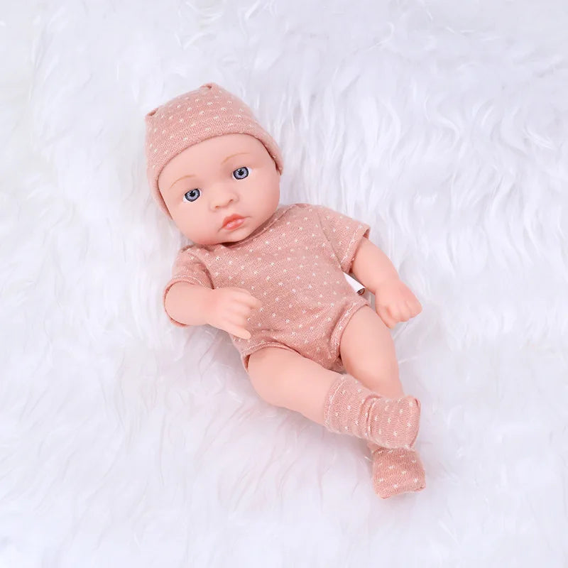 A realistic soft vinyl reborn baby doll wearing a matching pink patterned outfit and hat, lying on white fur.