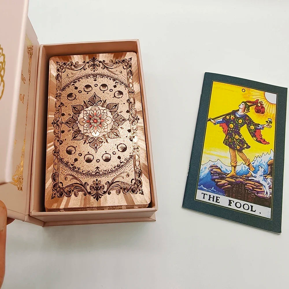 A gold foil tarot card is displayed inside a pink box, featuring an ornate design and the title The Fool.