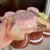A hand holds a realistic cake squishy fidget toy with pink and white frosting details.