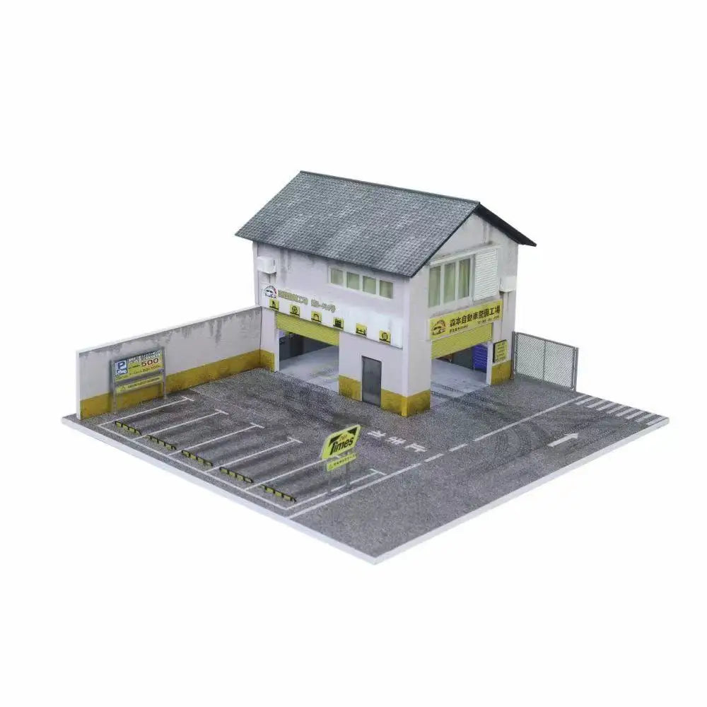 A miniature garage diorama for diecast cars featuring a small building and paved area.
