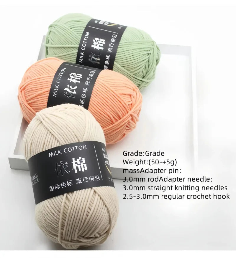 Three skeins of soft milk cotton yarn in light green, peach, and cream colors with labels indicating grade and weight.