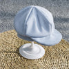 Light blue plaid knit romper and newsboy cap set displayed on a woven mat.