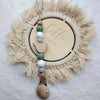 A wooden baby pacifier clip featuring silicone beads and a natural fiber wreath with the word hello world carved into the cen