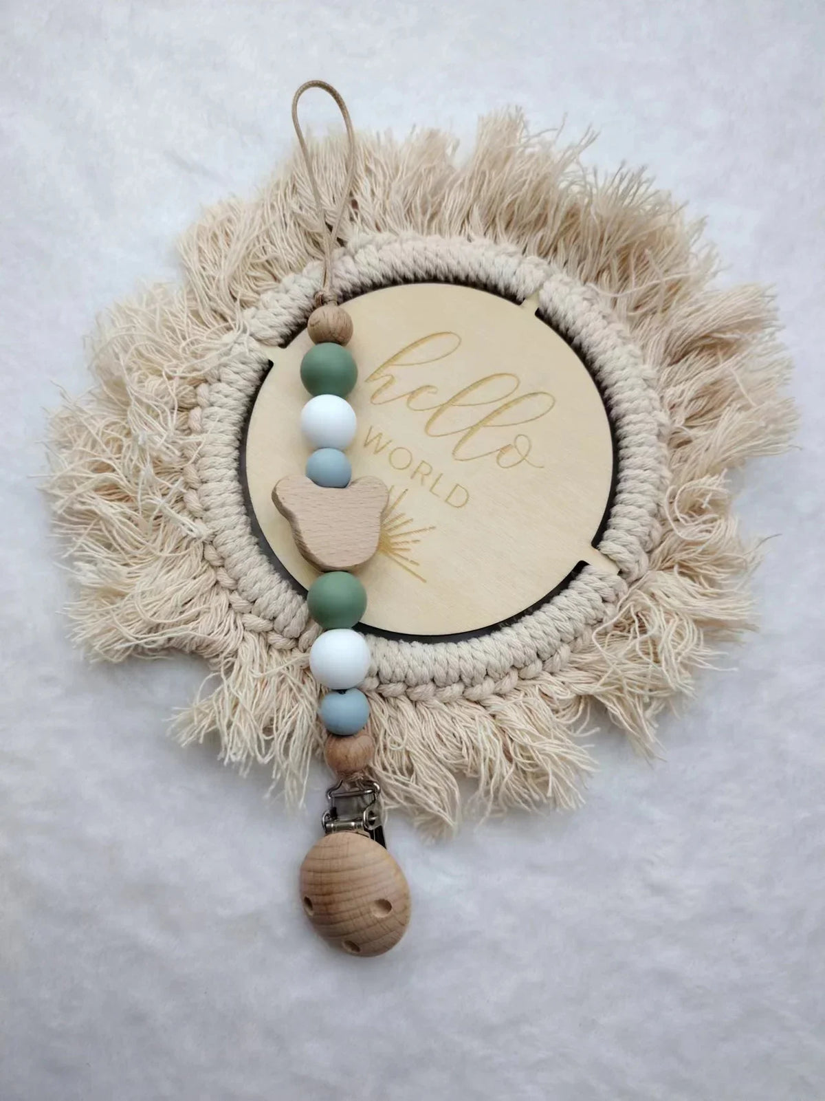 A wooden baby pacifier clip featuring silicone beads and a natural fiber wreath with the word hello world carved into the cen