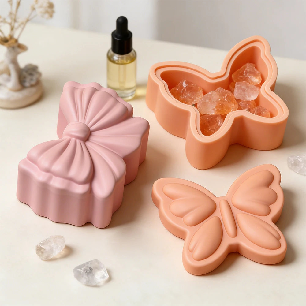A pink silicone resin mold shaped like a bowknot and a butterfly, with an amber glass bottle nearby.