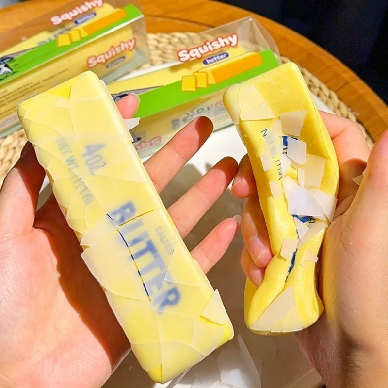 A hand holds a yellow squishy butter bar stress relief toy next to a box of the same product.