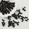 A pile of black oval glass rice grain beads is displayed on a white dish.